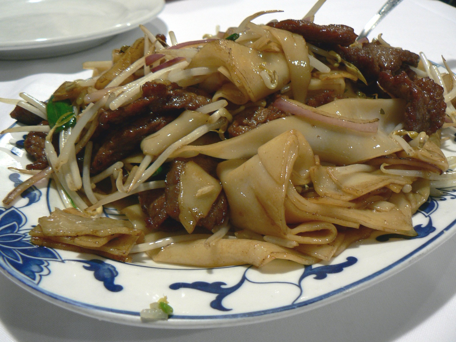 Beef chow fun on a blue-and-white porcelain plate with pale wide noodles, beef and bean sprouts
