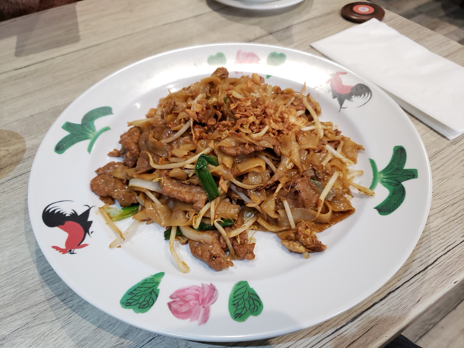 Beef chow fun served on a rooster-patterned plate with crispy fried shallots