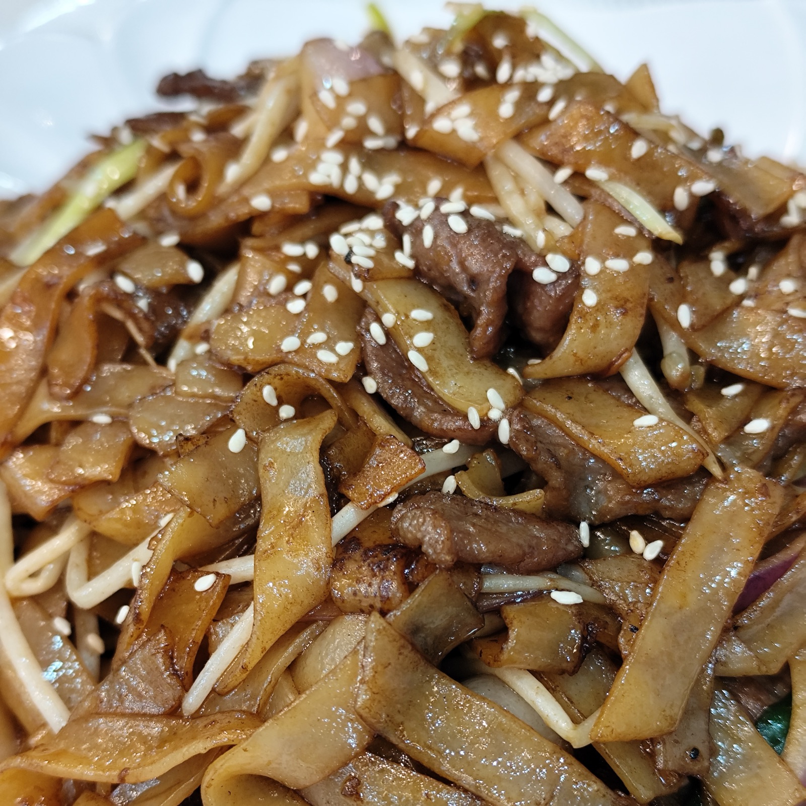 Macro detail of wide rice noodles, seared beef and bean sprouts glazed in dark soy